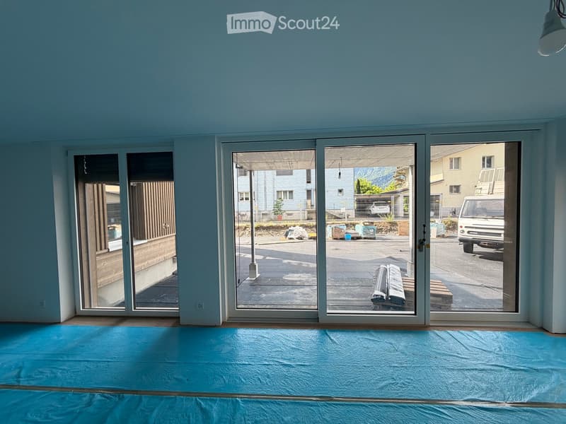 Empty room with light blue walls, large sliding glass doors leading to an outdoor area, and a blue protective sheet covering the floor.
