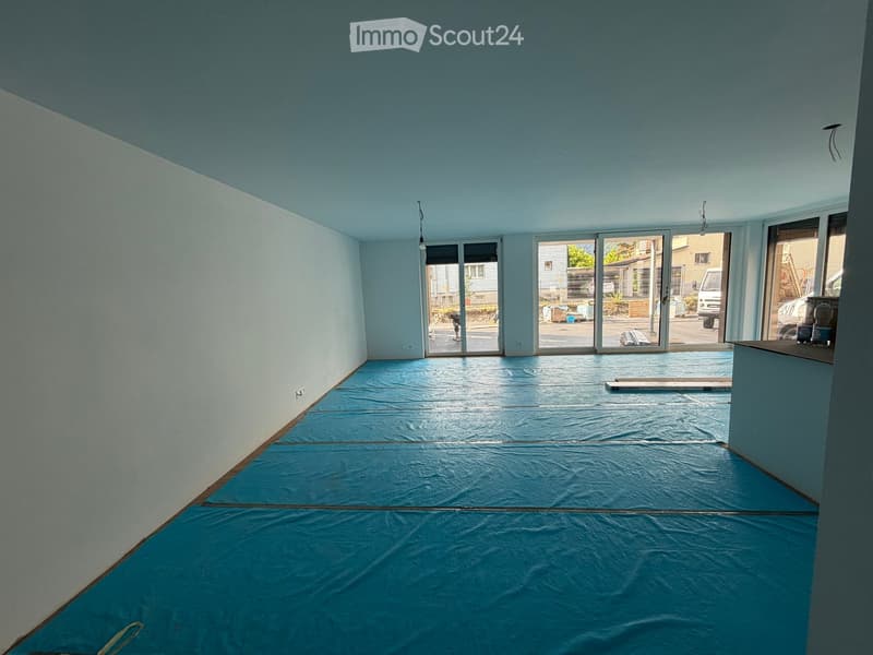 Empty room with light blue walls, a blue protective floor covering, and large sliding glass doors leading outside.