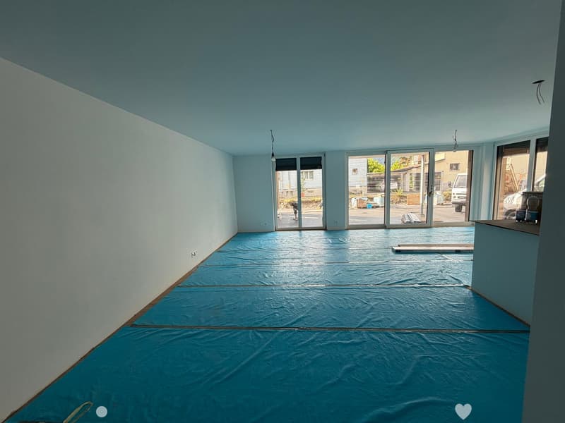 Empty room with light blue walls, a blue protective floor covering, and large sliding glass doors leading outside.
