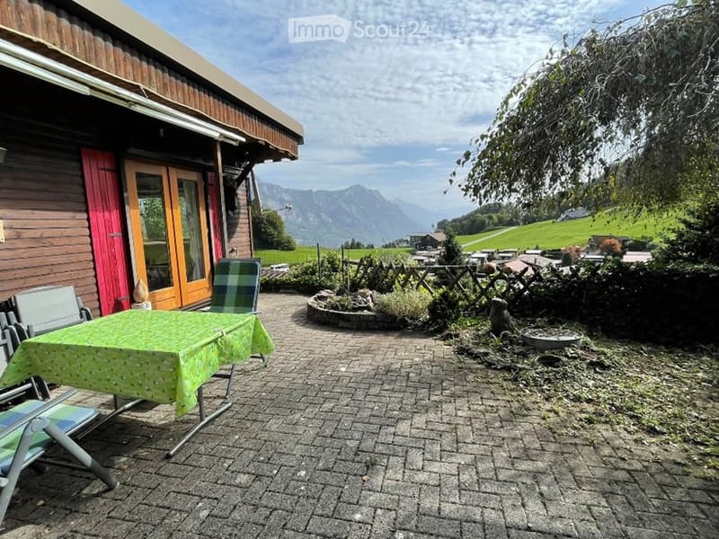 Outdoor patio with a table, chairs, and a view of mountains and greenery.
