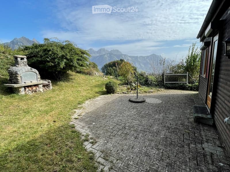 Garden area with a stone fireplace, grassy lawn, paved pathway, and scenic mountain view.