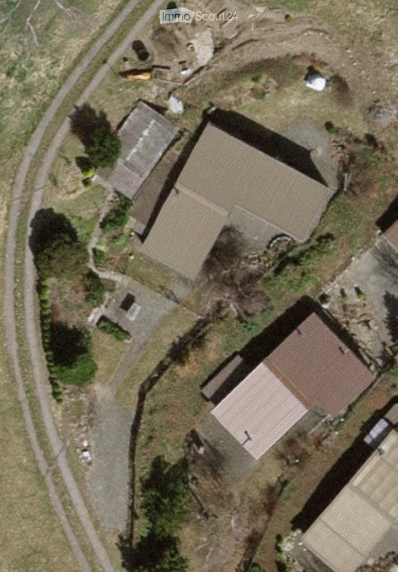 Aerial view of a residential complex with multiple buildings, including a main house and outbuildings, surrounded by a landscaped area with pathways and greenery.