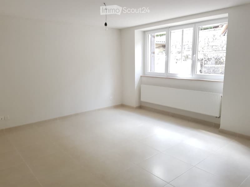 Empty room with white tiled floor, white walls, large window with radiator below, and visible electrical outlet.