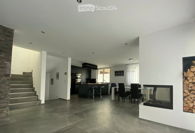Open-plan living and dining area with a modern fireplace, bar counter, dining table, and staircase leading to an upper level.