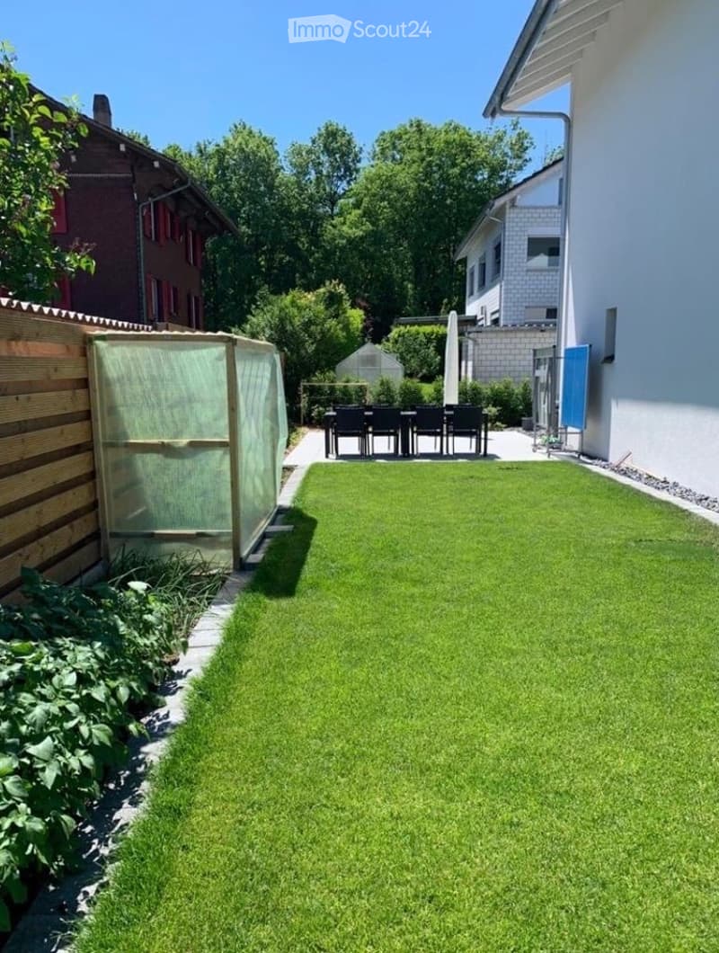 Well-maintained garden with a neatly trimmed lawn, wooden fence, outdoor dining set, and greenhouse.