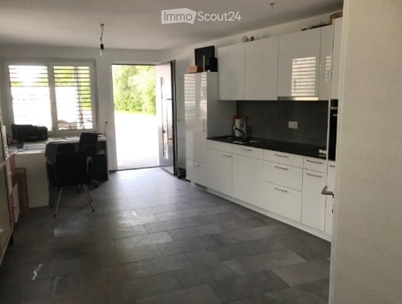 Modern kitchen with white cabinets, dark countertops, and a tiled floor. Features a refrigerator, sink, and a small dining area with a table and chairs.