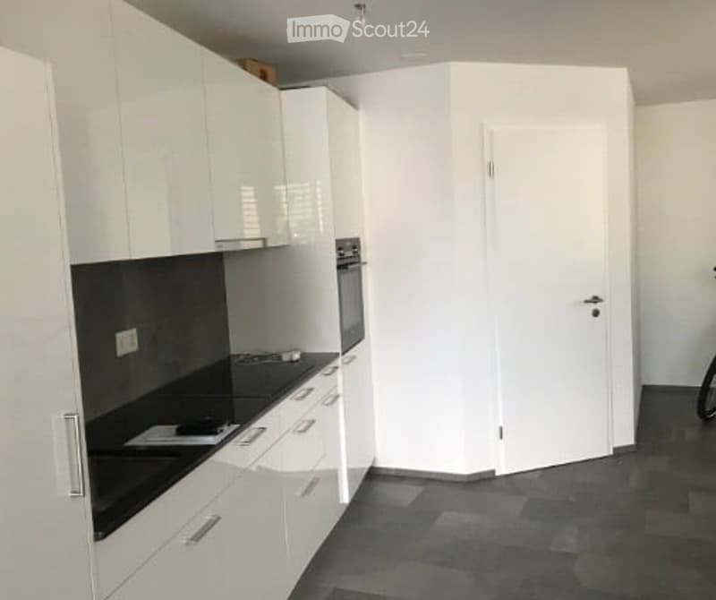 Modern kitchen with white cabinets, black countertop, and built-in oven. The space is clean and organized with a door leading to another room.