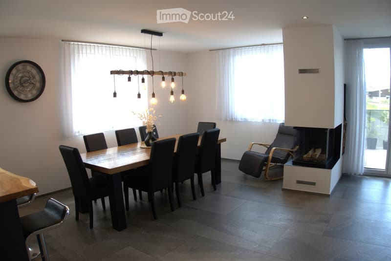 Modern dining room with a wooden dining table, black chairs, a fireplace, and a decorative clock on the wall.