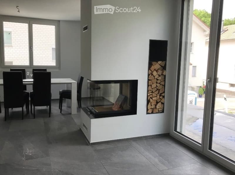 Modern dining area with a sleek white dining table, black chairs, and a built-in fireplace with a wood storage niche nearby.