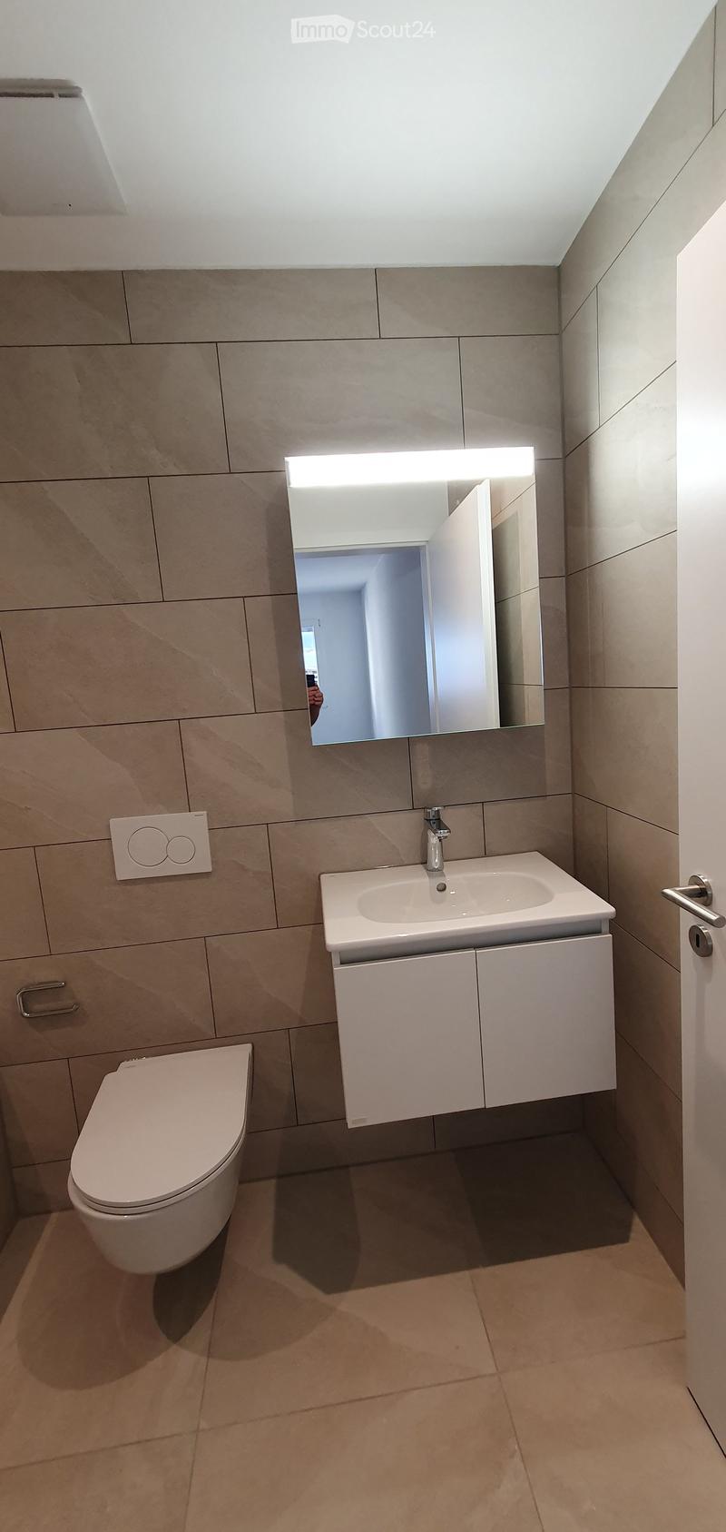 Modern bathroom with beige tiles, a toilet, a sink with a mirror, and a white cabinet.