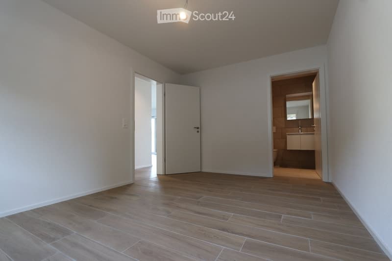 Empty room with wooden flooring and white walls, featuring two open doors leading to other spaces.