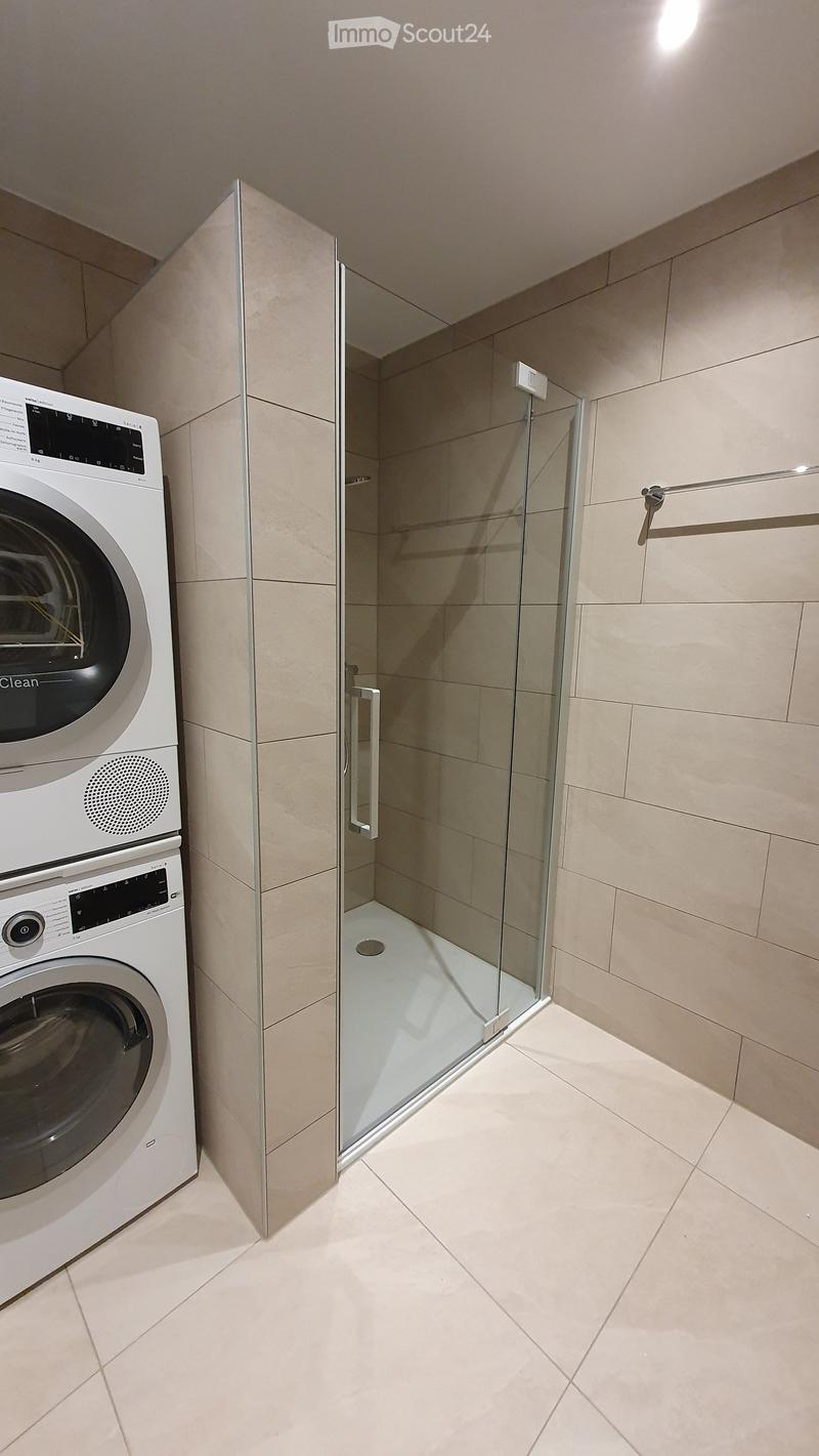 Modern bathroom with a glass-enclosed shower and a stacked washing machine/dryer unit.