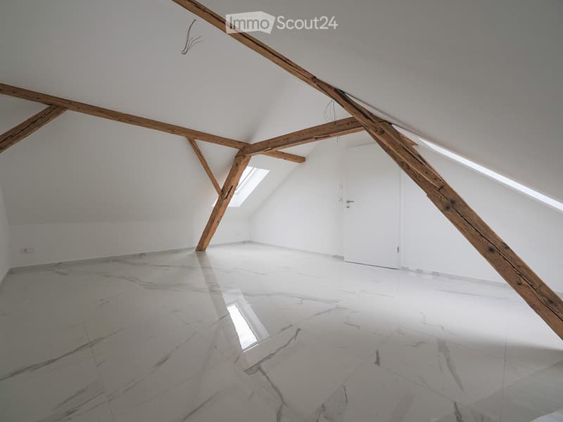 Empty attic space with exposed wooden beams, white walls, and a polished marble floor. Skylights allow natural light to enter.