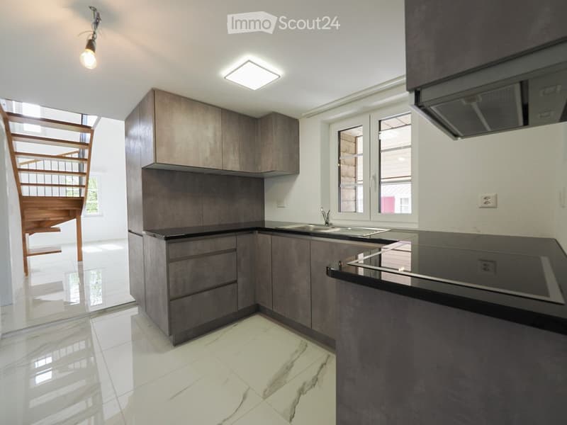 Modern kitchen with dark grey cabinets, white tiled floor, and a black countertop. Features a sink, faucet, and built-in lighting.
