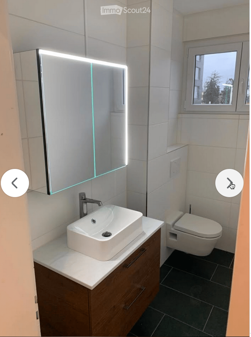 Modern bathroom with a white sink, sleek faucet, illuminated mirror, wooden cabinet, and toilet.