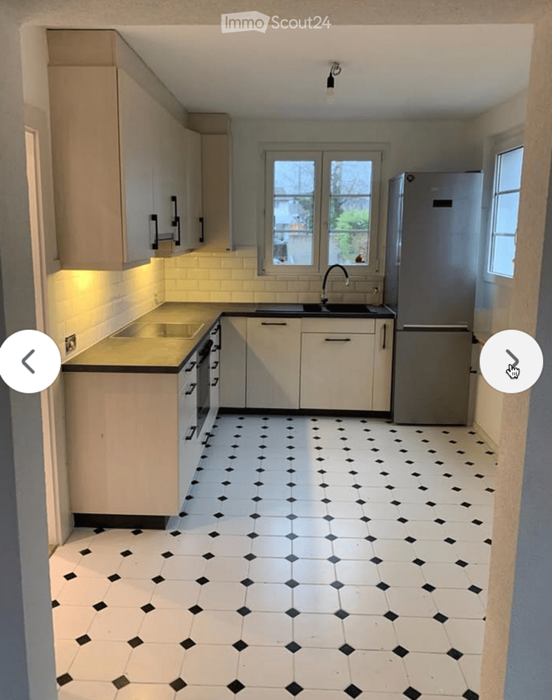 Modern kitchen with white cabinets, black countertops, and a stainless steel refrigerator. The floor features a classic black and white tiled pattern.