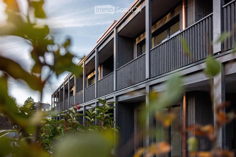 Modern building with multiple floors, wooden and metal balconies, and large windows.