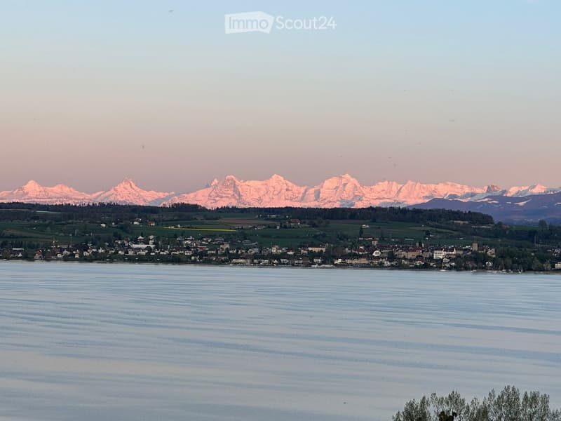 Scenic view of a lake with a town on the shore and snow-capped mountains in the background.