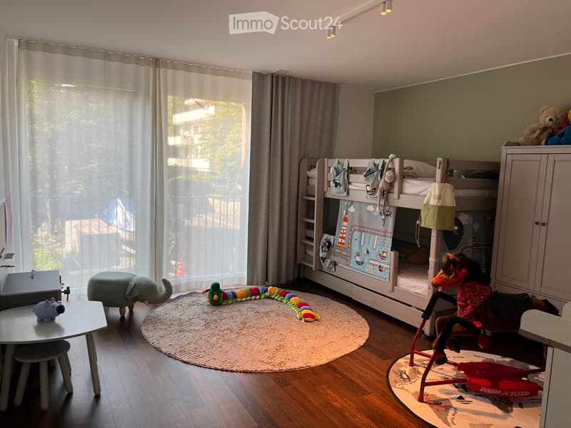 Brightly lit children's bedroom with bunk bed, toys, and a round rug. Features a toy horse, toy elephant, toy caterpillar, and a small table with a toy hippo.