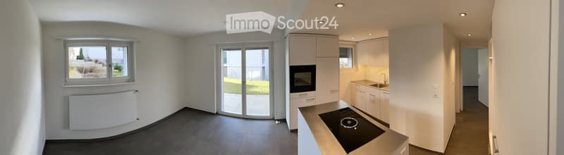 Modern, minimalist kitchen with white cabinets, a built-in oven, a sink, and a radiator. The space features large windows and a sliding glass door leading to an outdoor area.