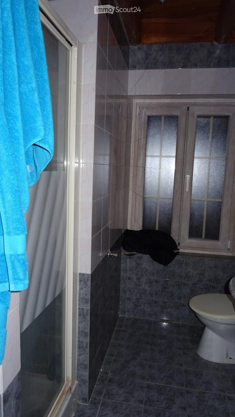 Modern bathroom with dark grey tiles, a glass shower enclosure, a white toilet, and a blue towel hanging on the side.