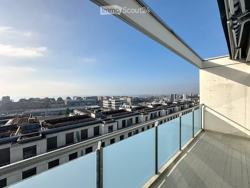 Roof terrace with glass balustrade, overlooking a cityscape with buildings and distant skyline.