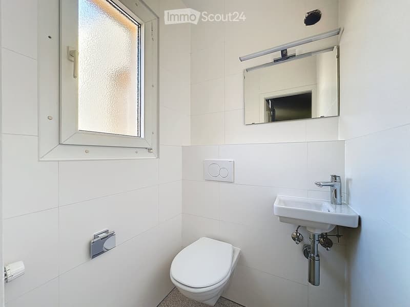 Modern bathroom with white tiles, a toilet, a sink with a modern faucet, and a mirror above the sink.