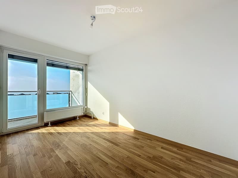 Empty room with wooden flooring, white walls, large windows, and a radiator. No furniture or equipment present.