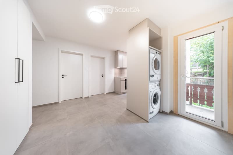 Modern, minimalist hallway with a built-in washing machine, kitchen cabinets, and a sliding glass door leading to a balcony.