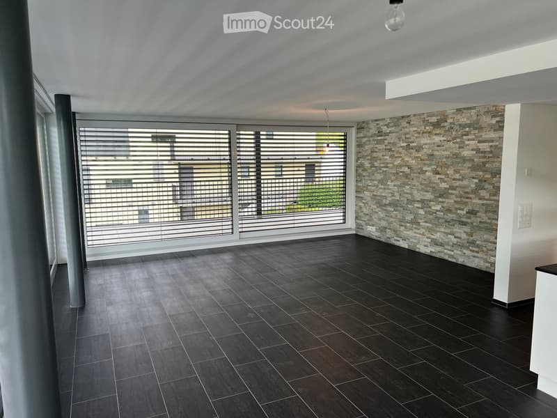 Empty room with dark tiled flooring, large windows with blinds, and a textured stone accent wall.
