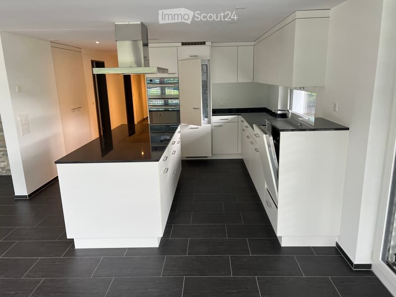 Modern kitchen with white cabinets, black countertops, and black tiled flooring. Features a central island, built-in oven, and range hood.