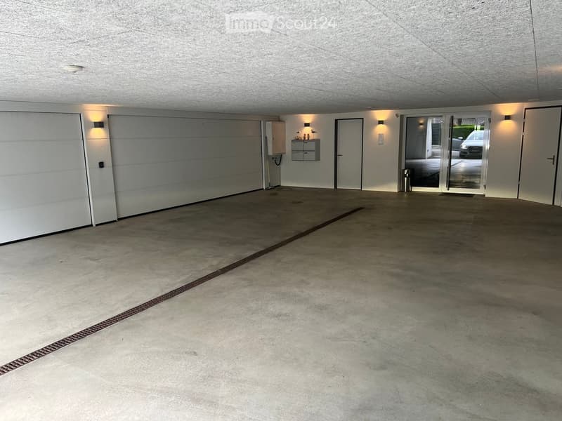 Empty underground garage with concrete floor, white walls, and a large garage door on the left side.