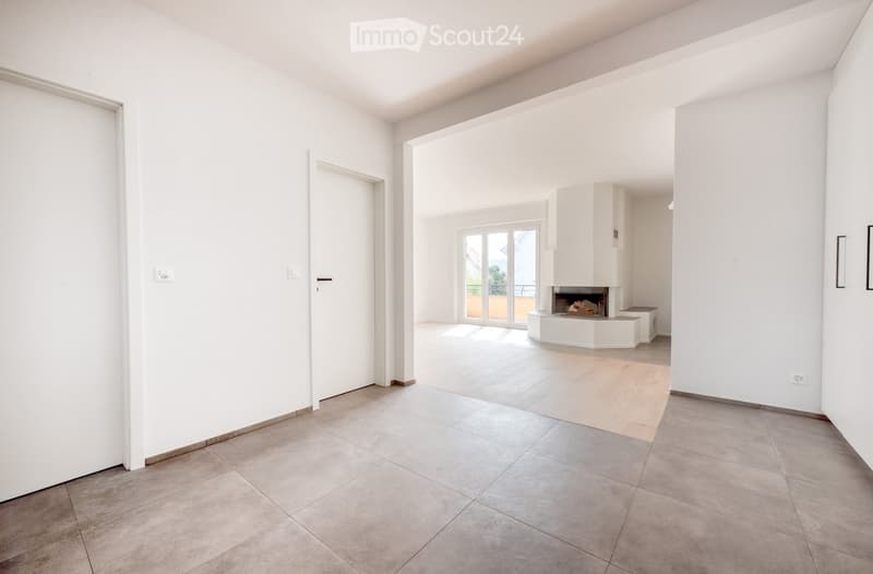 Empty living space with tiled floor, white walls, fireplace, and sliding glass door leading to a balcony.