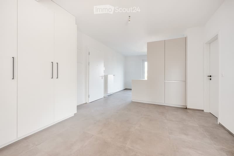 Empty room with white walls, tiled floor, built-in white wardrobes, and a doorway leading to another space.