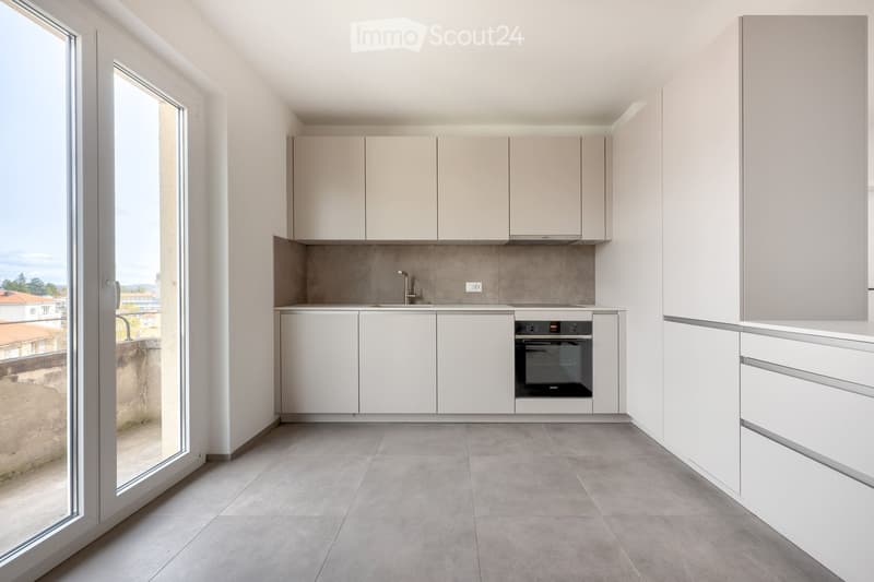 Modern kitchen with white cabinets, a built-in oven, and a sleek faucet, featuring large windows that offer a view of the surrounding area.