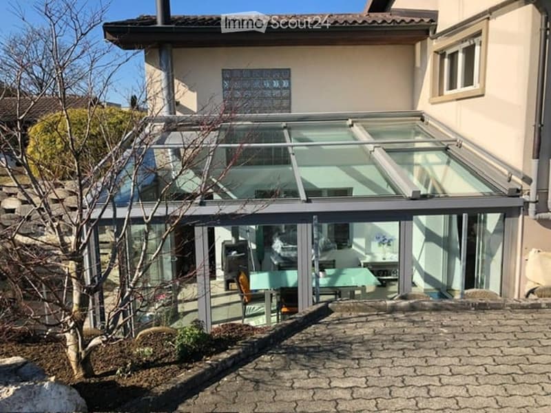 Modern house with a large glass balcony/terraces attached to the main structure, featuring a sleek design and contemporary architecture.