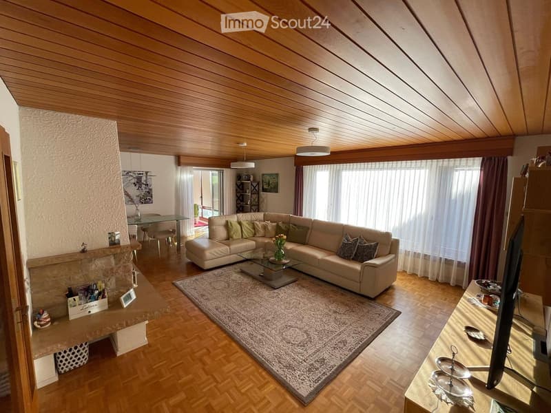 Modern living room with wooden floors, a large sectional sofa, coffee table, TV, dining area, and fireplace.