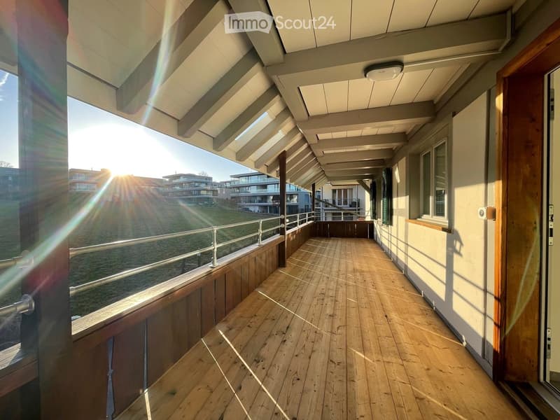 Wooden balcony with metal railing, overlooking a grassy area and modern buildings in the distance.