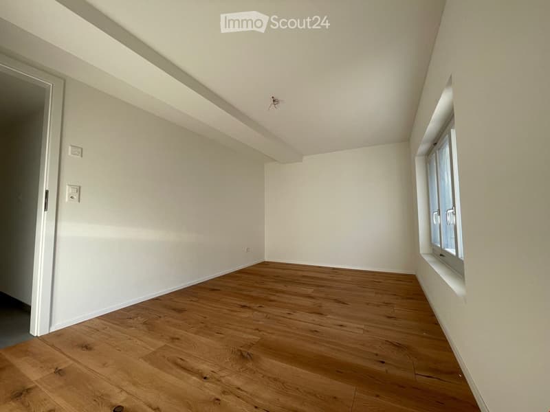 Empty room with wooden flooring, white walls, and a window with white frames. The ceiling has a sloped design typical of an attic space.