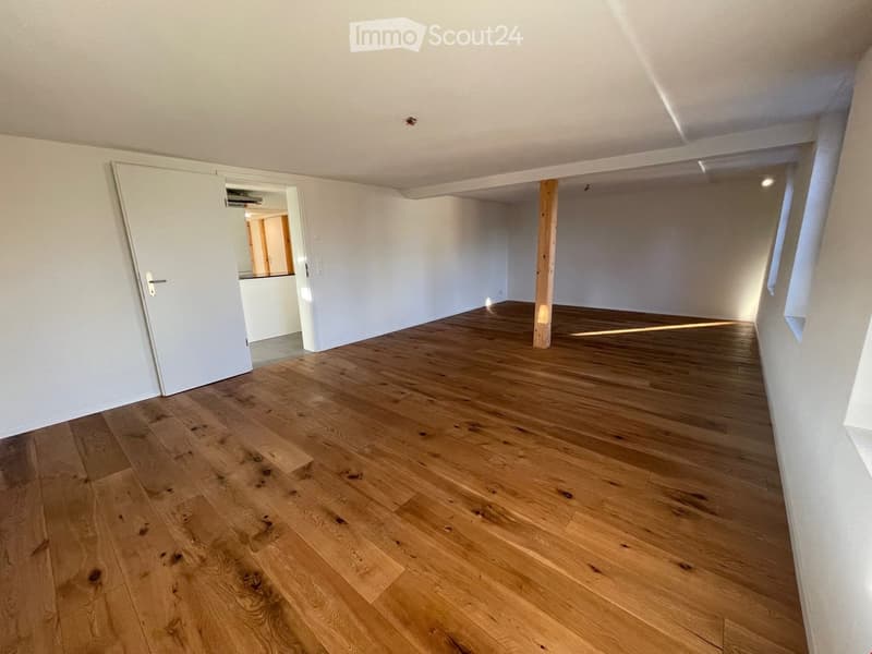 Empty room with light wooden flooring and white walls, featuring a doorway leading to another area.