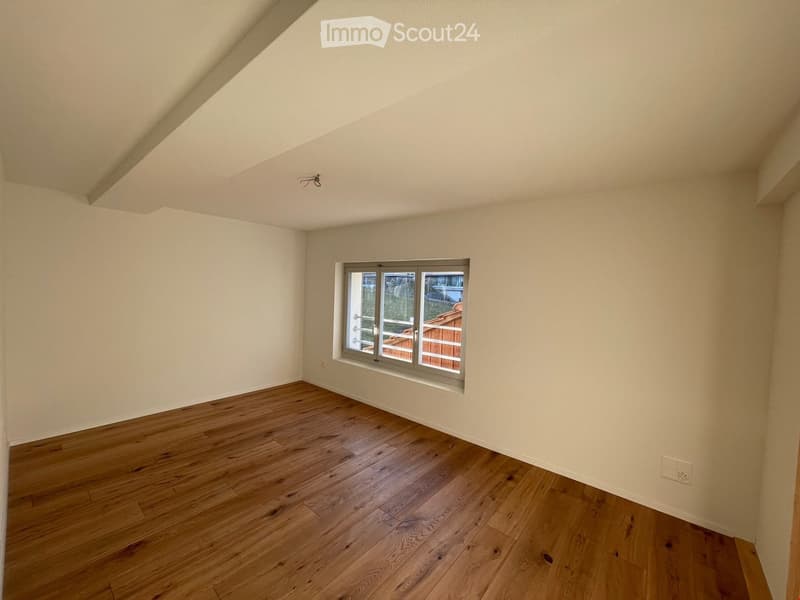 Empty room with wooden flooring, white walls, and a single window with a view of an outdoor deck.