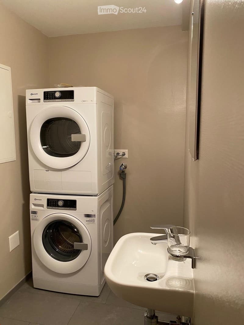 Bathroom with a stacked washing machine and dryer unit, a white sink with a glass cup on the counter.