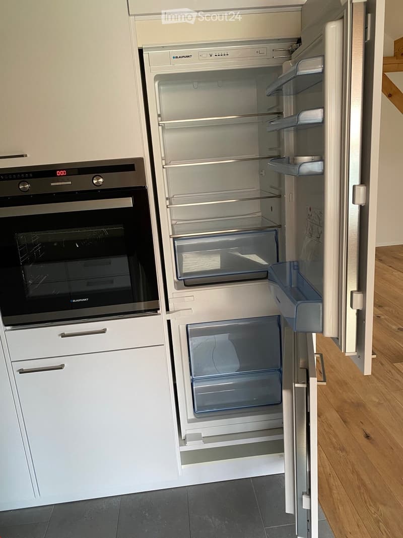 Modern kitchen with white cabinets, an open refrigerator, and a built-in oven. The refrigerator is empty, and the oven is closed.