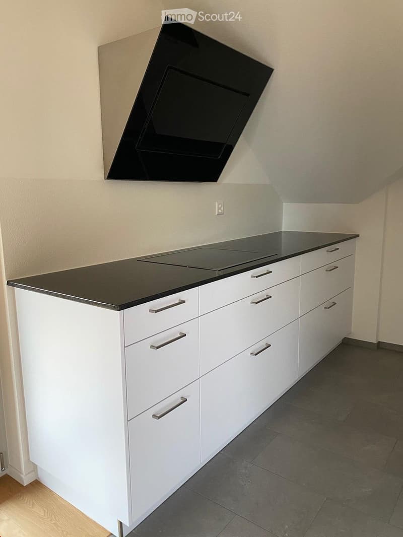 Modern kitchen with white cabinets, black countertop, induction cooktop, and sleek stainless steel handles.