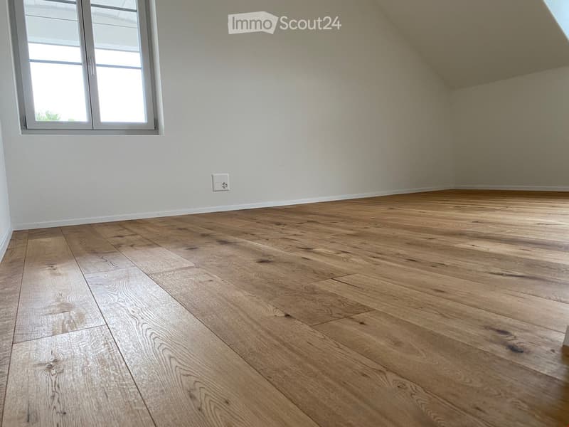 Empty room with wooden flooring and white walls, featuring a large window with white frame and a light switch on the wall.