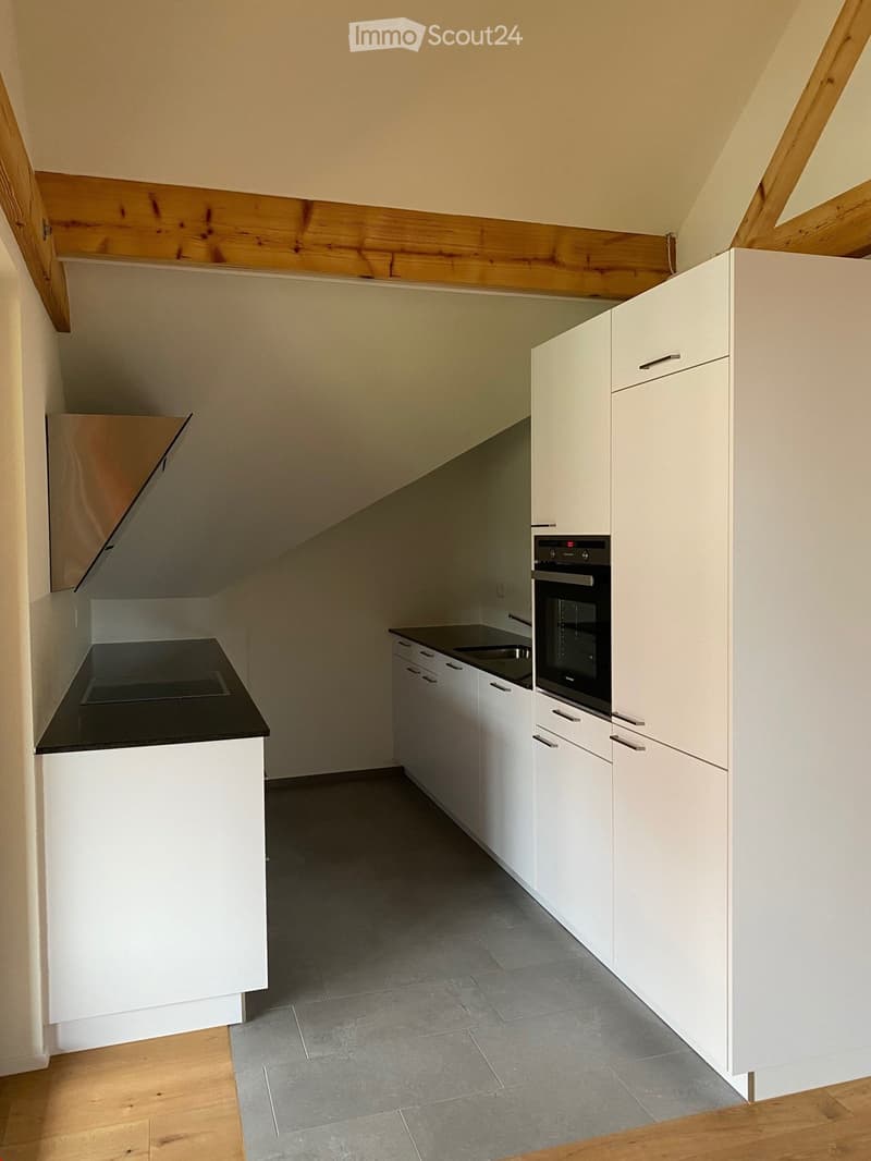 Modern kitchen with white cabinets, black countertop, and built-in oven. The space features a sleek design with a mix of wooden and tiled flooring.
