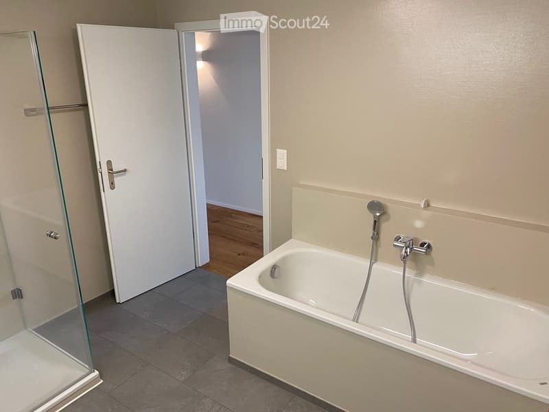 Modern bathroom with a bathtub, glass shower enclosure, and tiled floor.
