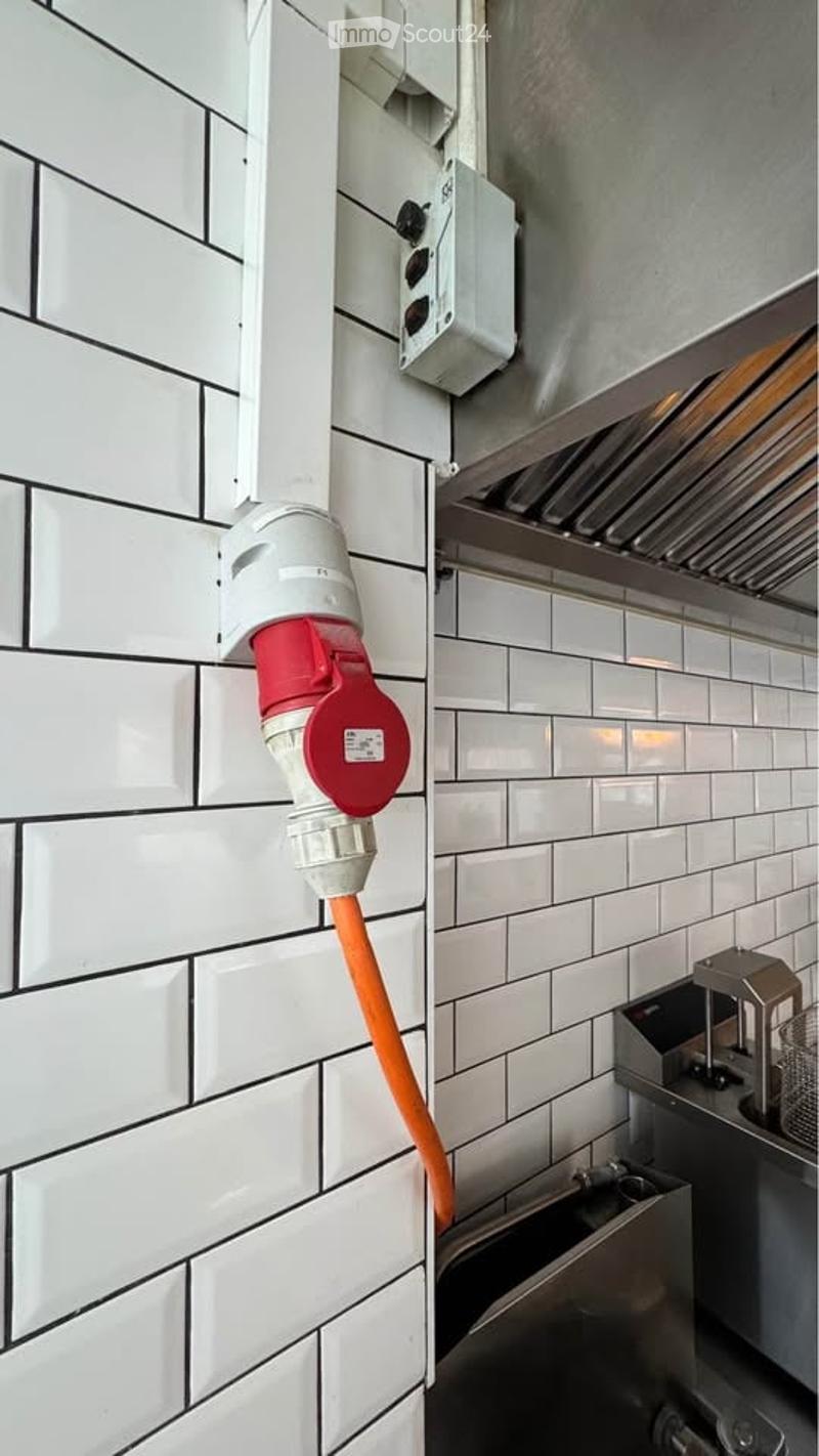 A close-up view of a kitchen wall with a white tiled surface, featuring a red and white electrical outlet and a grey vent hood above.