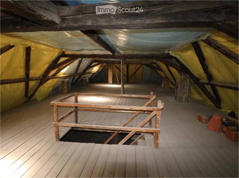 Empty attic space with wooden beams, exposed wooden floor, and a small opening in the floor. No furniture or equipment present.
