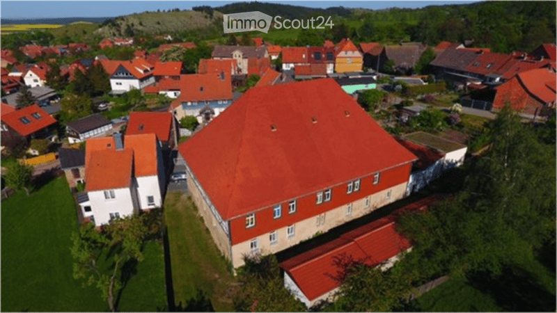 Aerial view of a rural village with multiple houses, red-tiled roofs, and scattered greenery.